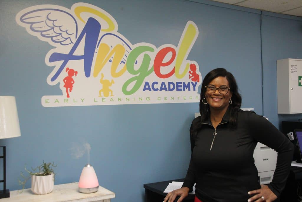 Tracy Smith stands in front of her Angel Academy Early Learning Centers Logo
