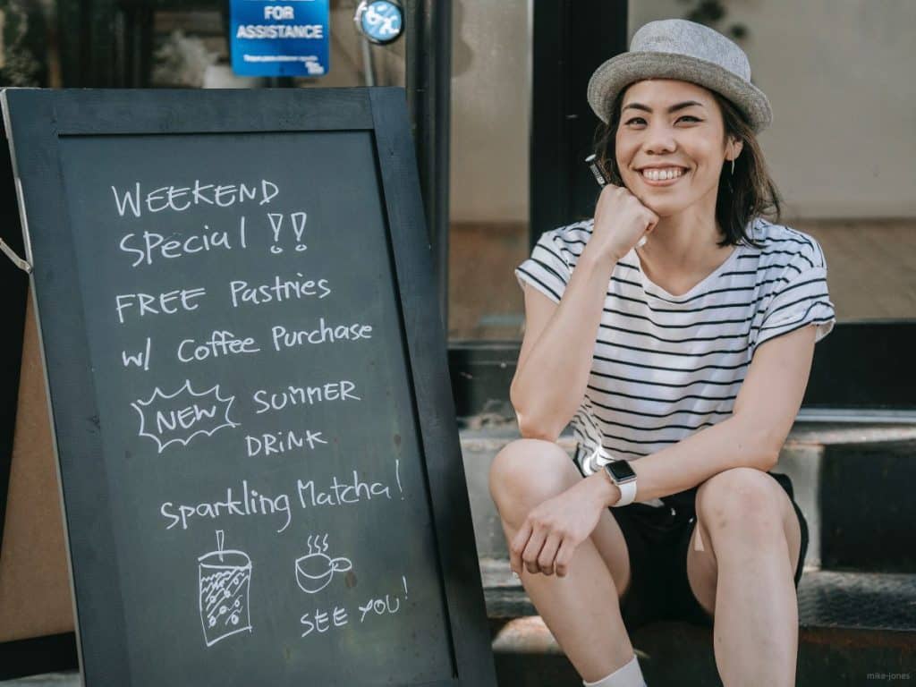 Person sitting next to a chalkboard sign with special pricing listed